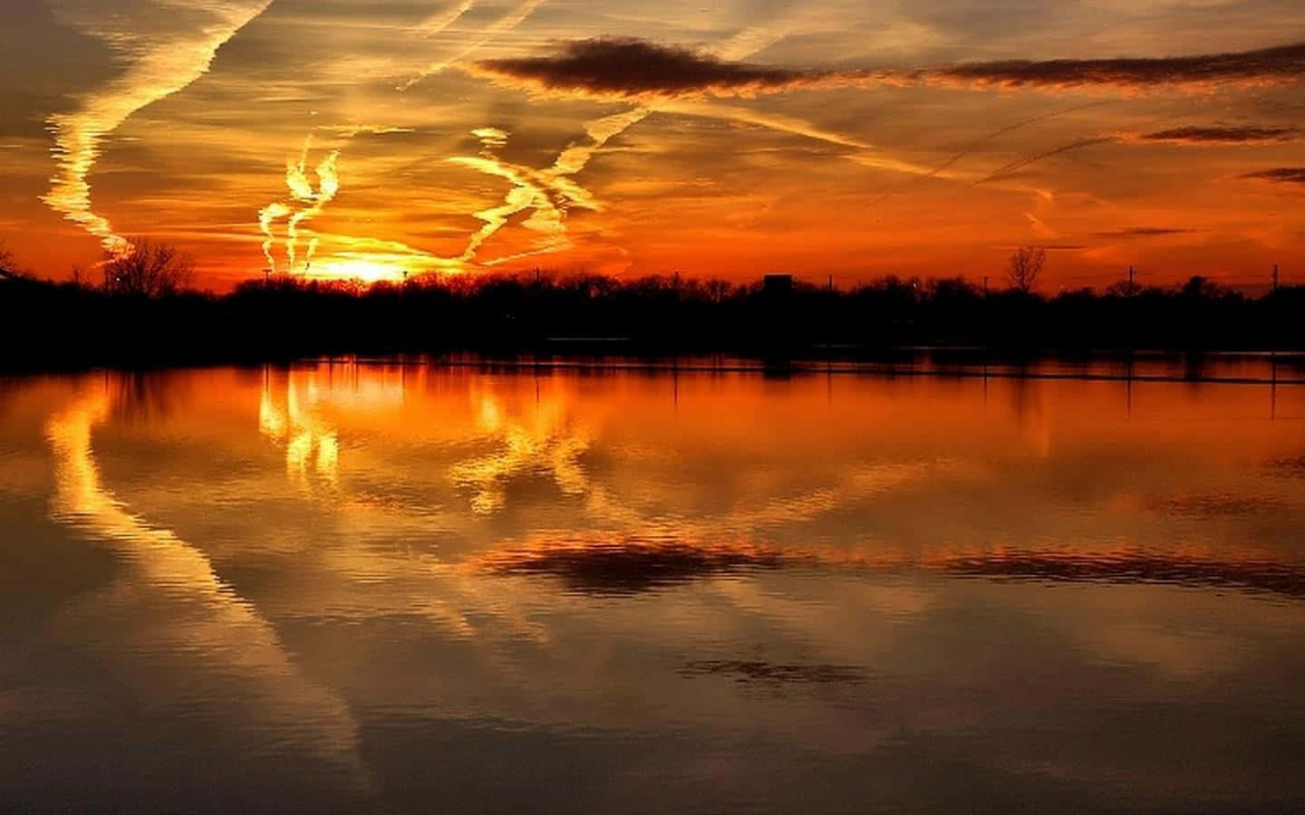Sunset Reflection 桌布 壁紙 — 熾熱的夕陽將天空染成橙色和紅色，完美地倒映在平靜的湖面上，湖岸邊有樹木的剪影。
