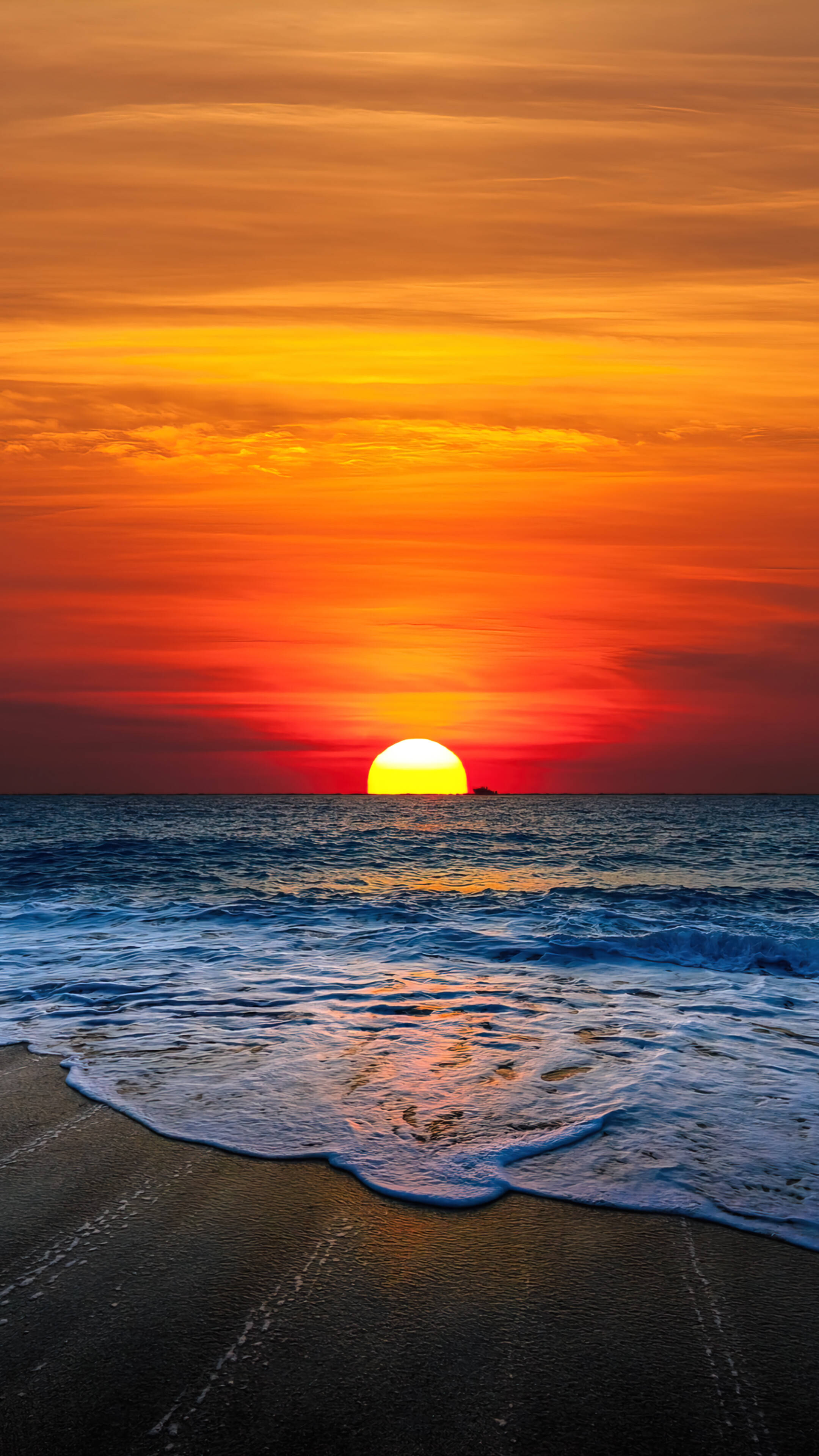 夕陽映照海洋，海浪沖刷深色沙灘。 — 日落天空 壁紙