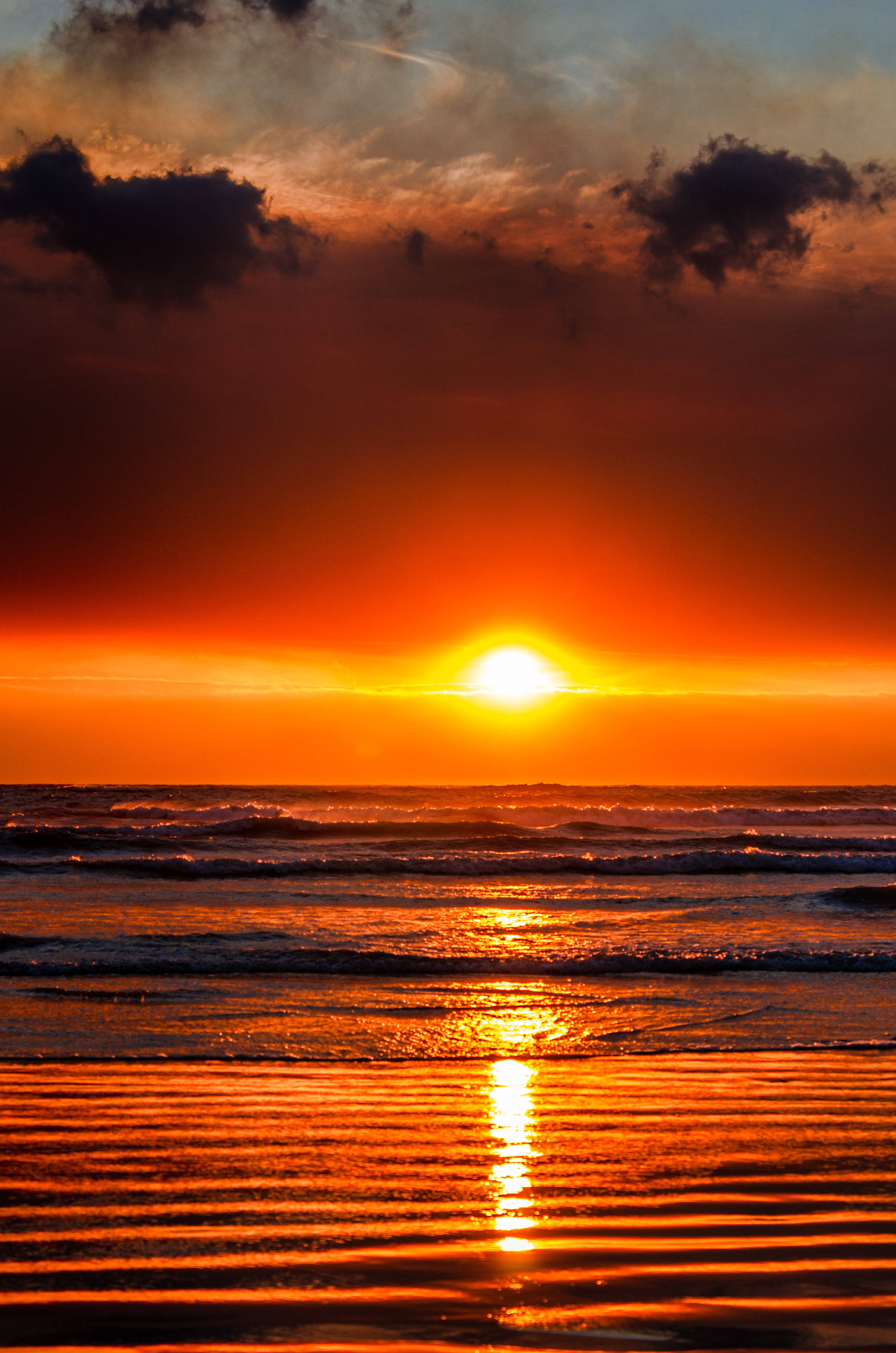 波浪 桌布 壁紙 — 熾熱的夕陽將海洋和濕沙染成鮮豔的橙色，海浪在戲劇性的雲層下翻滾。