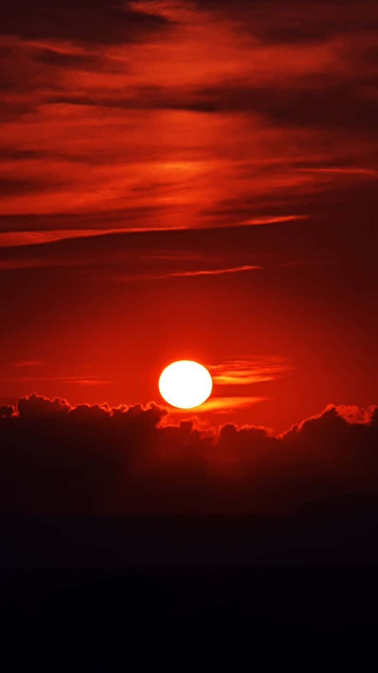 Red Sunset 桌布 壁紙 — 熾熱的太陽在火紅的天空中落下，在烏雲和遠處的大地上投下戲劇性的陰影。