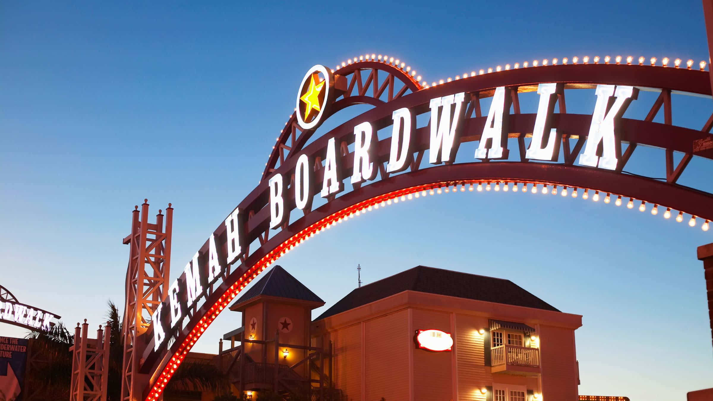 德州 桌布 壁紙 — 燈光明亮的 Kemah Boardwalk 拱門在暮色天空下閃耀，溫暖的燈光勾勒出它的結構。
