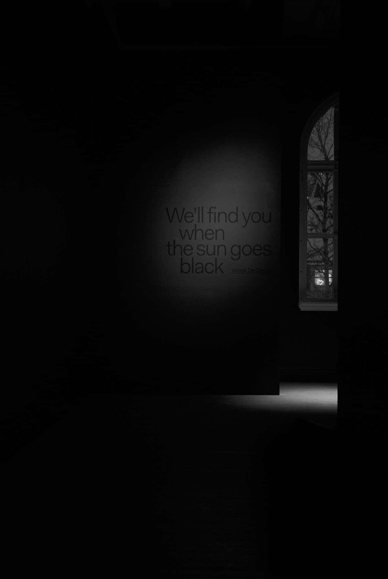 Dark Corner 桌布 壁紙 — 燈光昏暗的房間，牆上投射著一句引言，狹窄的窗戶顯示外面光禿禿的樹木。