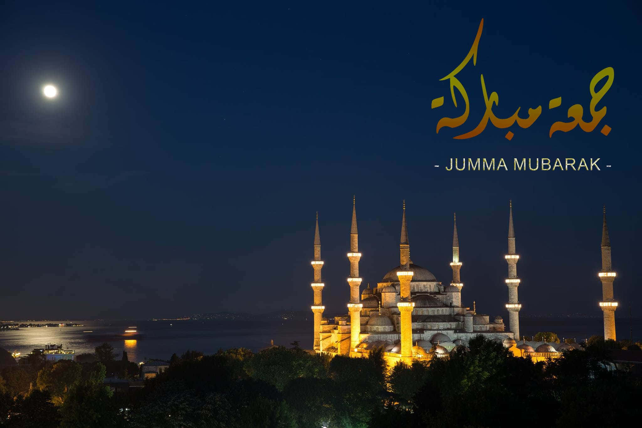 Jumma Mubarak 桌布 壁紙 — 燈火通明的藍色清真寺，六座宣禮塔在明亮的月光下，在漆黑的夜空中閃耀，並帶有「Jumma Mubarak」文字。