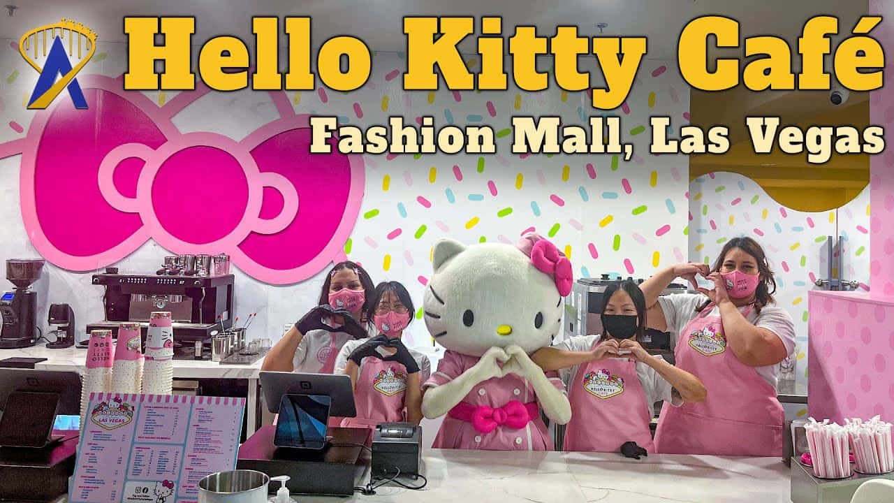 燦爛微笑的 Hello Kitty 壁紙 — 員工和一個巨大的Hello Kitty吉祥物在明亮的招牌下，於粉紅色咖啡櫃檯後面擺出心形手勢。