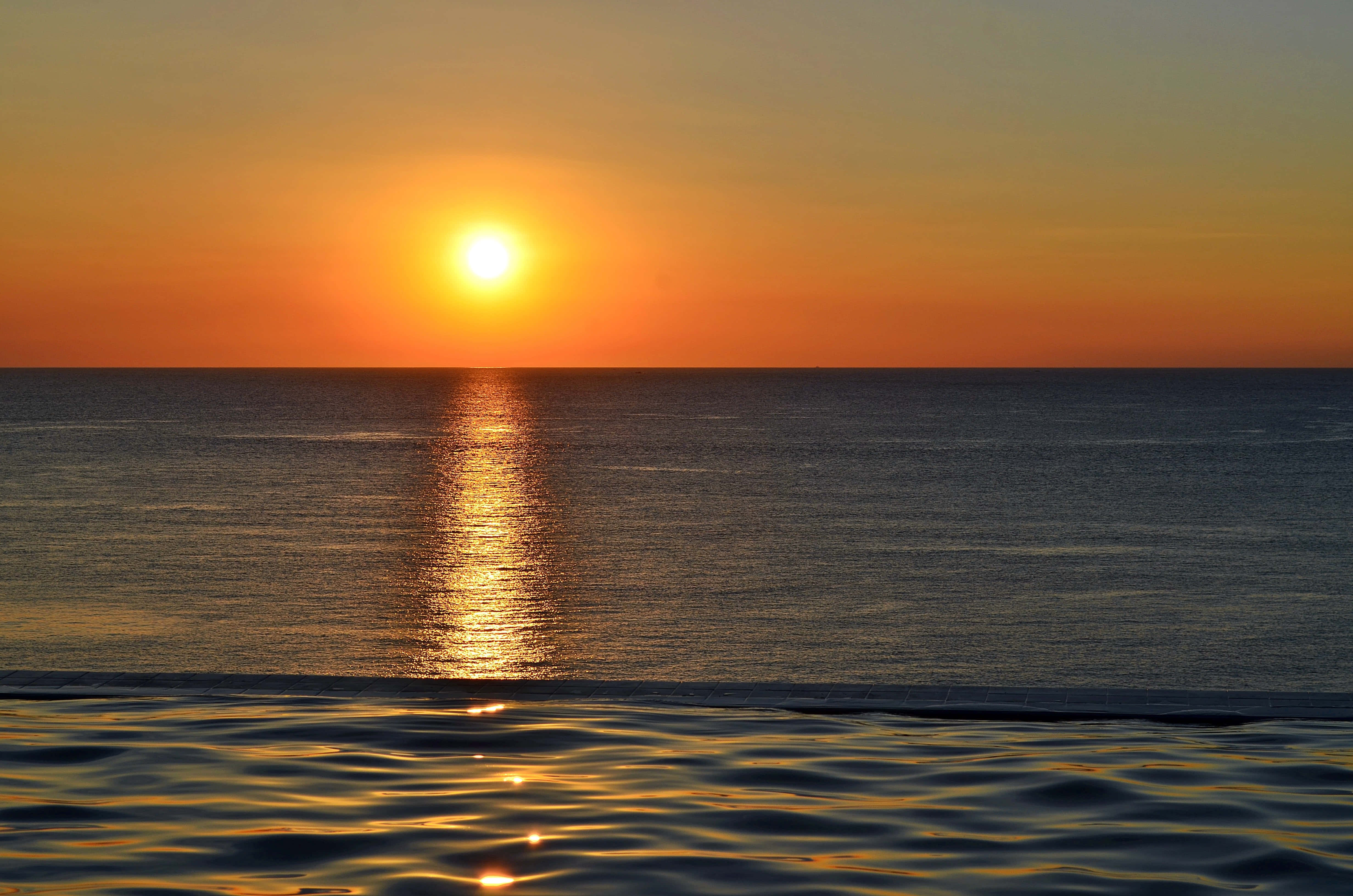 Sunset Ocean 桌布 壁紙 — 燦爛的夕陽將金色光芒灑在平靜的海面上，閃爍的倒影一直延伸到地平線。