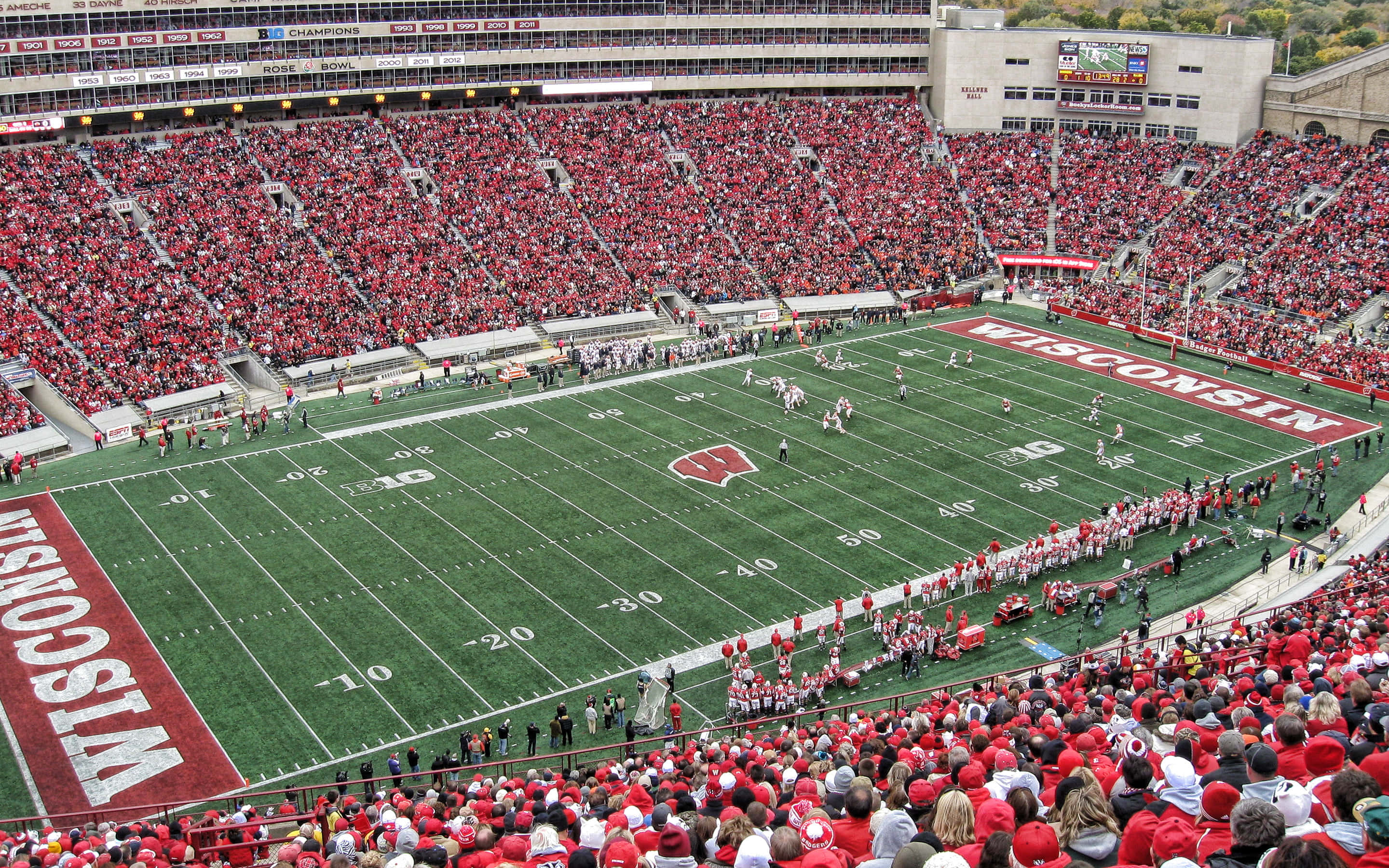 Wisconsin Badgers 桌布 壁紙 — 爆滿足球場的鳥瞰圖，身穿紅色衣服的球迷正在歡呼，球員在綠色場地上比賽。