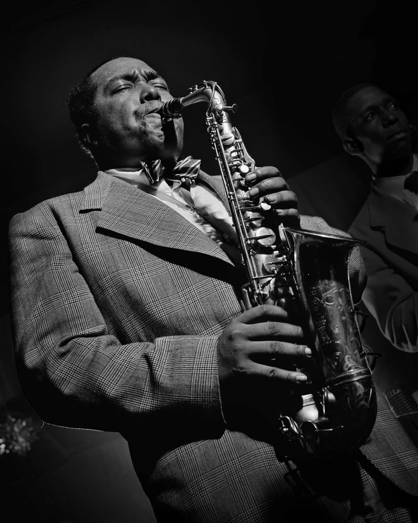 爵士音樂家查理·帕克 壁紙 — 一位身穿格紋西裝的爵士薩克斯風手，在戲劇性的舞台燈光下熱情演奏他的樂器。
