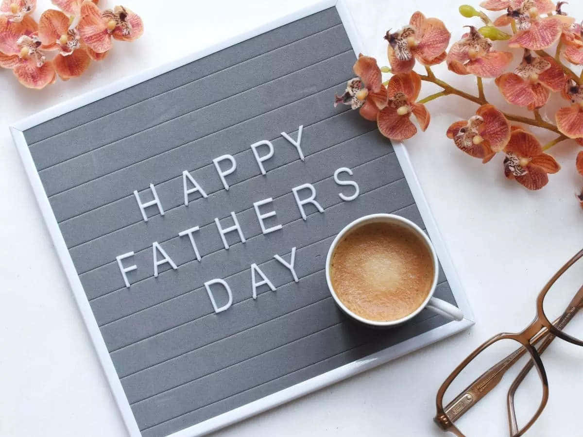 父親節禮品卡圖 壁紙 — 灰色字母板上顯示「HAPPY FATHERS DAY」，周圍環繞著粉紅色蘭花、一杯咖啡和眼鏡，放在白色表面上。