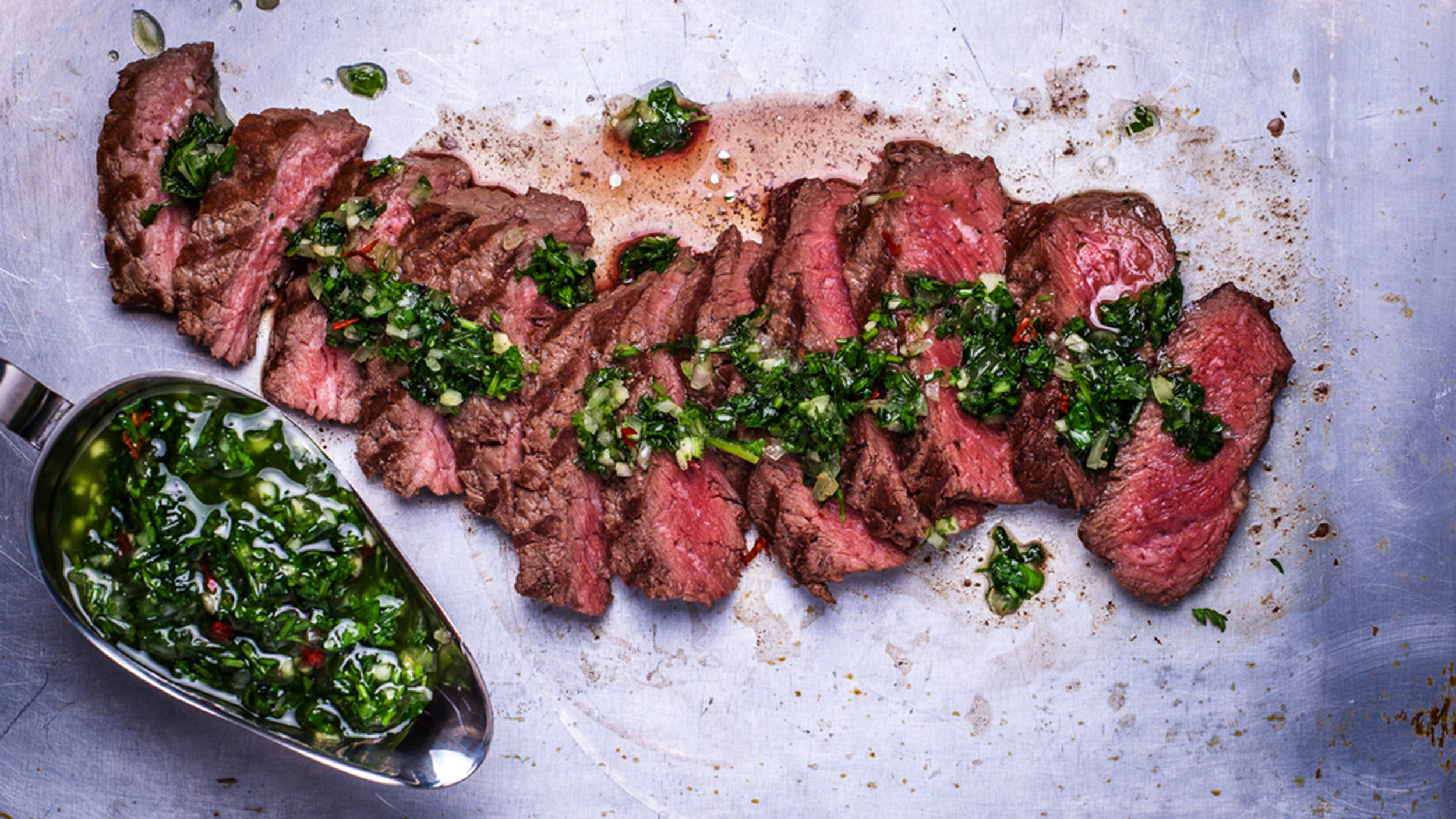 牛腹肉巴西烤肉 壁紙 — 切片中等熟度牛排，配上新鮮的阿根廷青醬，放在金屬托盤上。