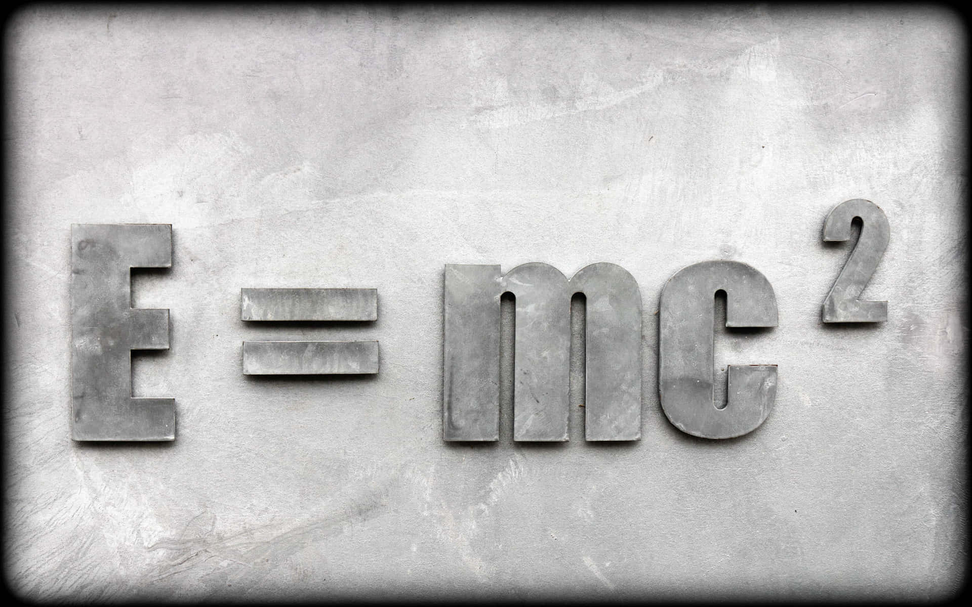 在紋理混凝土表面上以凸起金屬字母呈現的E=mc²公式。