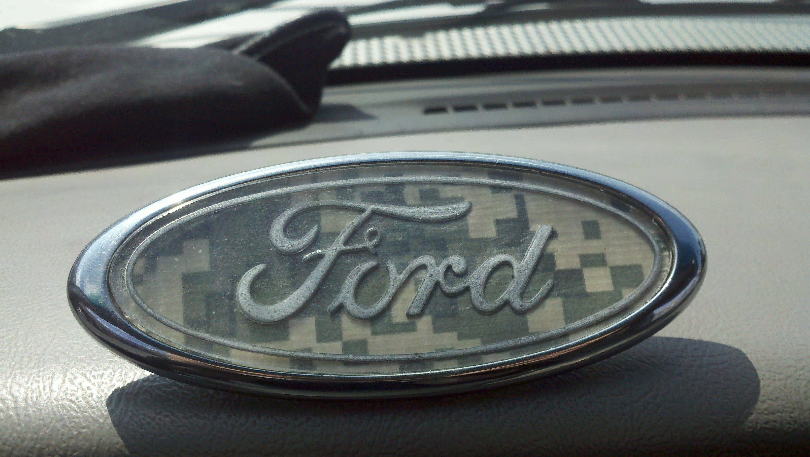 Ford Logo 桌布 壁紙 — 特寫：日光下汽車儀表板上帶迷彩圖案的福特標誌。