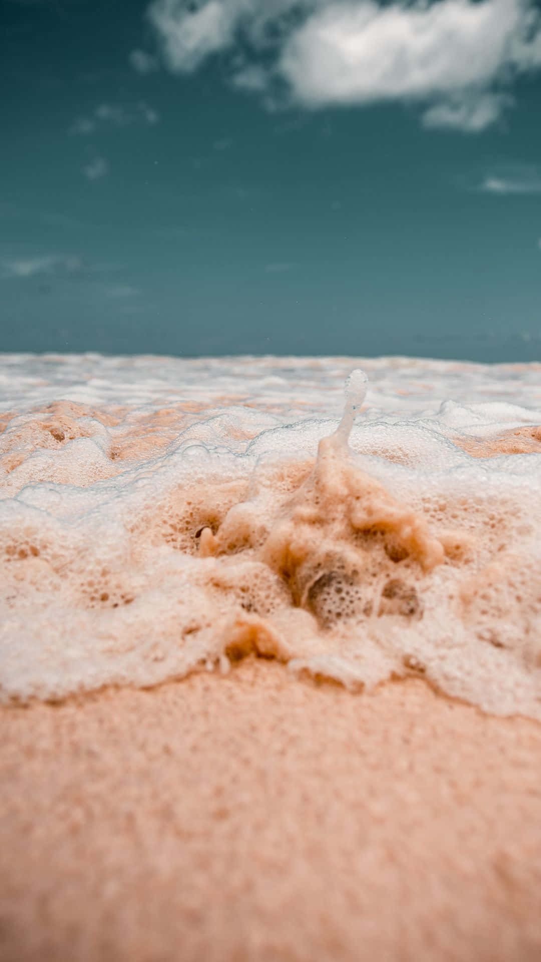 Pink Beach 桌布 壁紙 — 特寫：粉紅色海浪泡沫在沙灘上翻湧，天空呈青綠色，雲朵散佈。