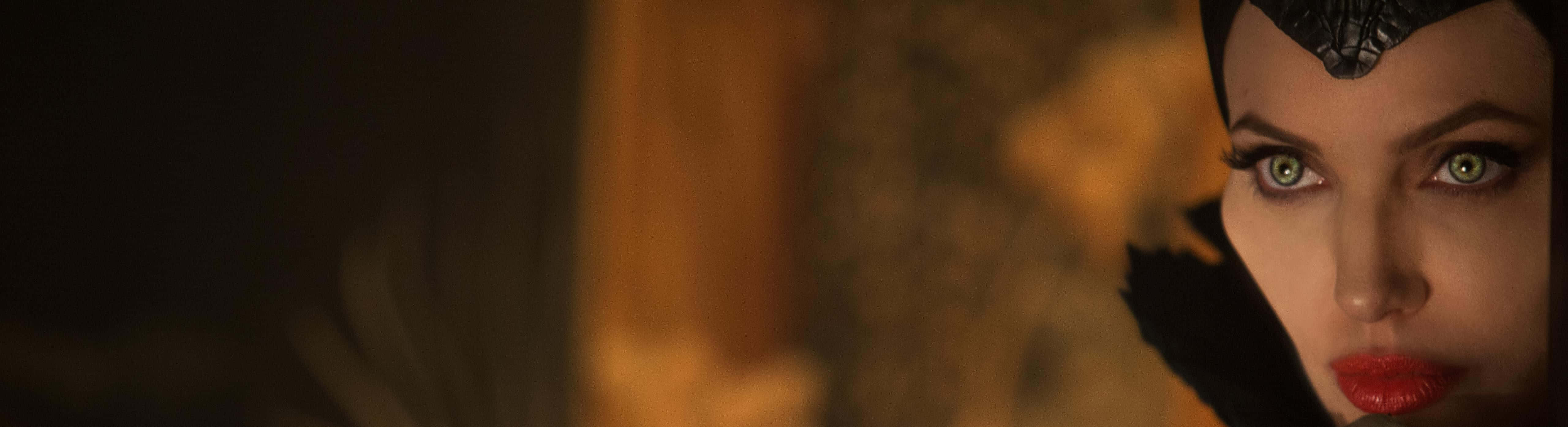 Evil Witch 桌布 壁紙 — 特寫一位擁有引人注目的綠色眼睛和紅唇的女性，在溫暖昏暗的燈光下戴著黑色華麗頭飾。
