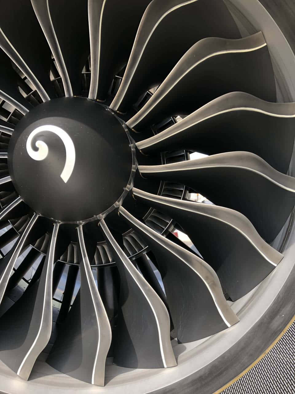 Jet Engine 桌布 壁紙 — 特寫一個時尚的噴射引擎風扇，黑色中心帶有白色螺旋標誌，背景為金屬葉片。