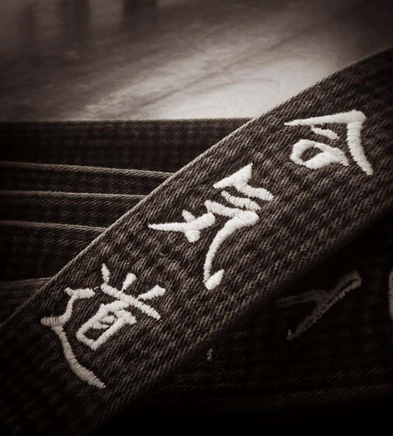 Martial Arts Uniform 桌布 壁紙 — 特寫一個深色紋理武術腰帶，帶有白色刺繡漢字，背景柔和模糊。