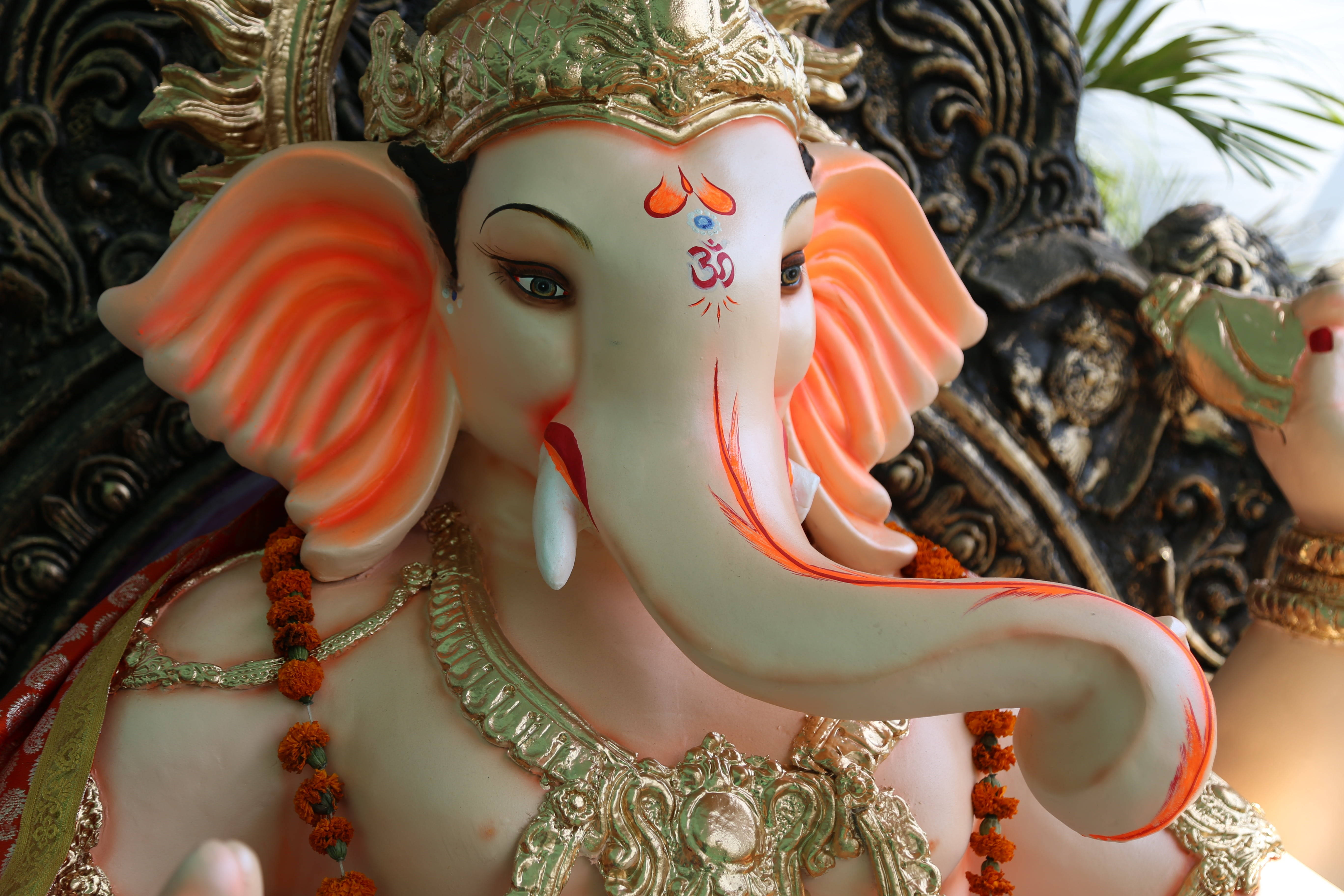Ganesh Chaturthi 桌布 壁紙 — 特寫一個精細的白色象頭神像，飾有金色皇冠和橙色點綴，背景是華麗的深色。