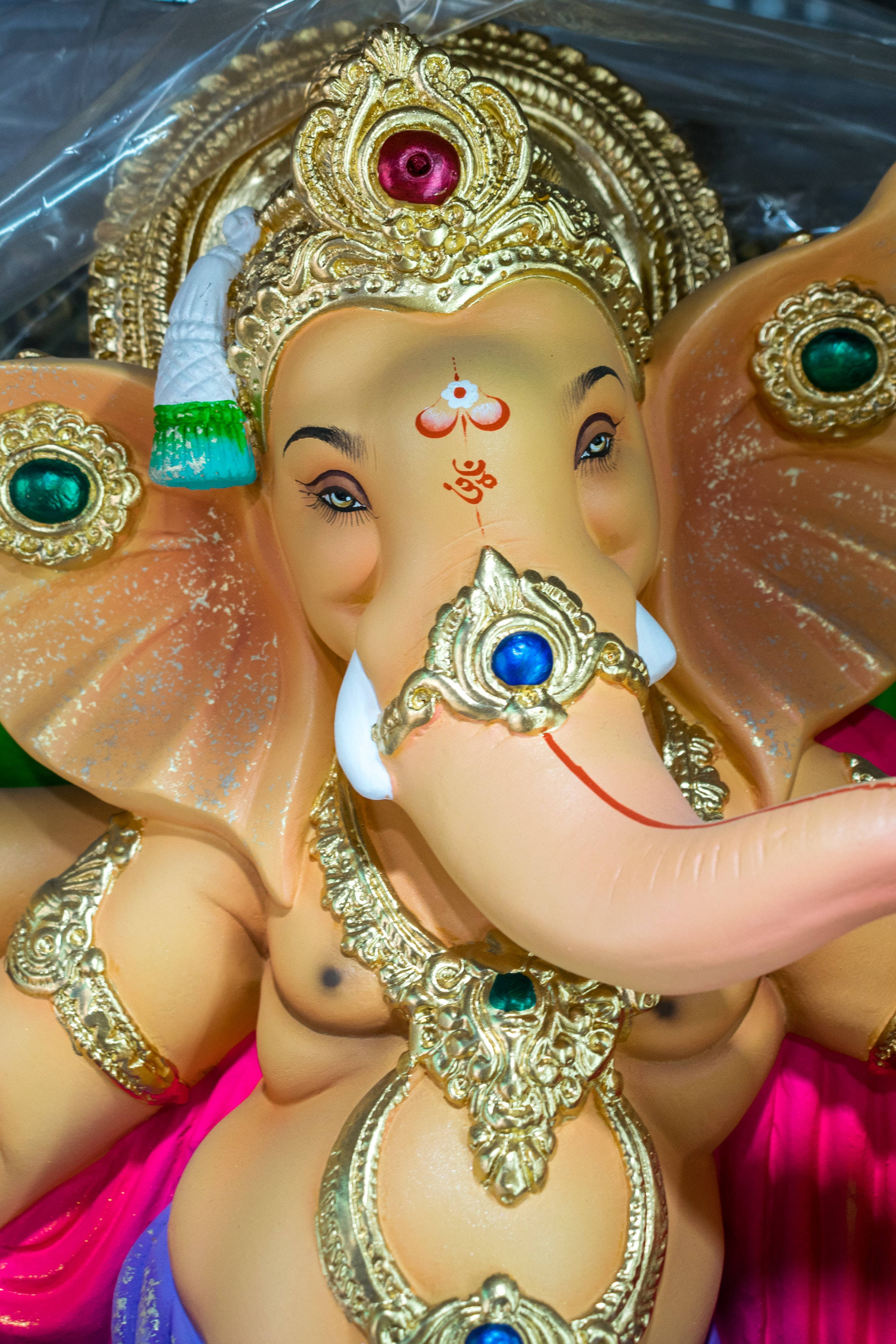 Ganesh 桌布 壁紙 — 特寫一個色彩繽紛的塑料象神雕像，飾有黃金珠寶和寶石，背景為塑料。