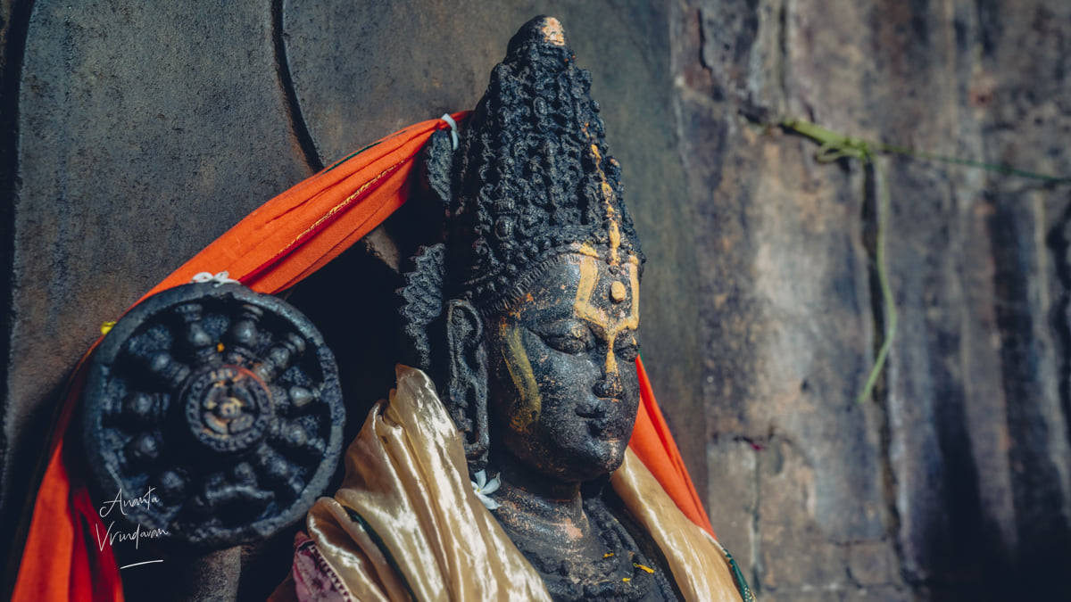 Statue Aesthetic 桌布 壁紙 — 特寫一個風化的黑色佛像，披著鮮豔的橙色和金色布料，靠著紋理石牆。
