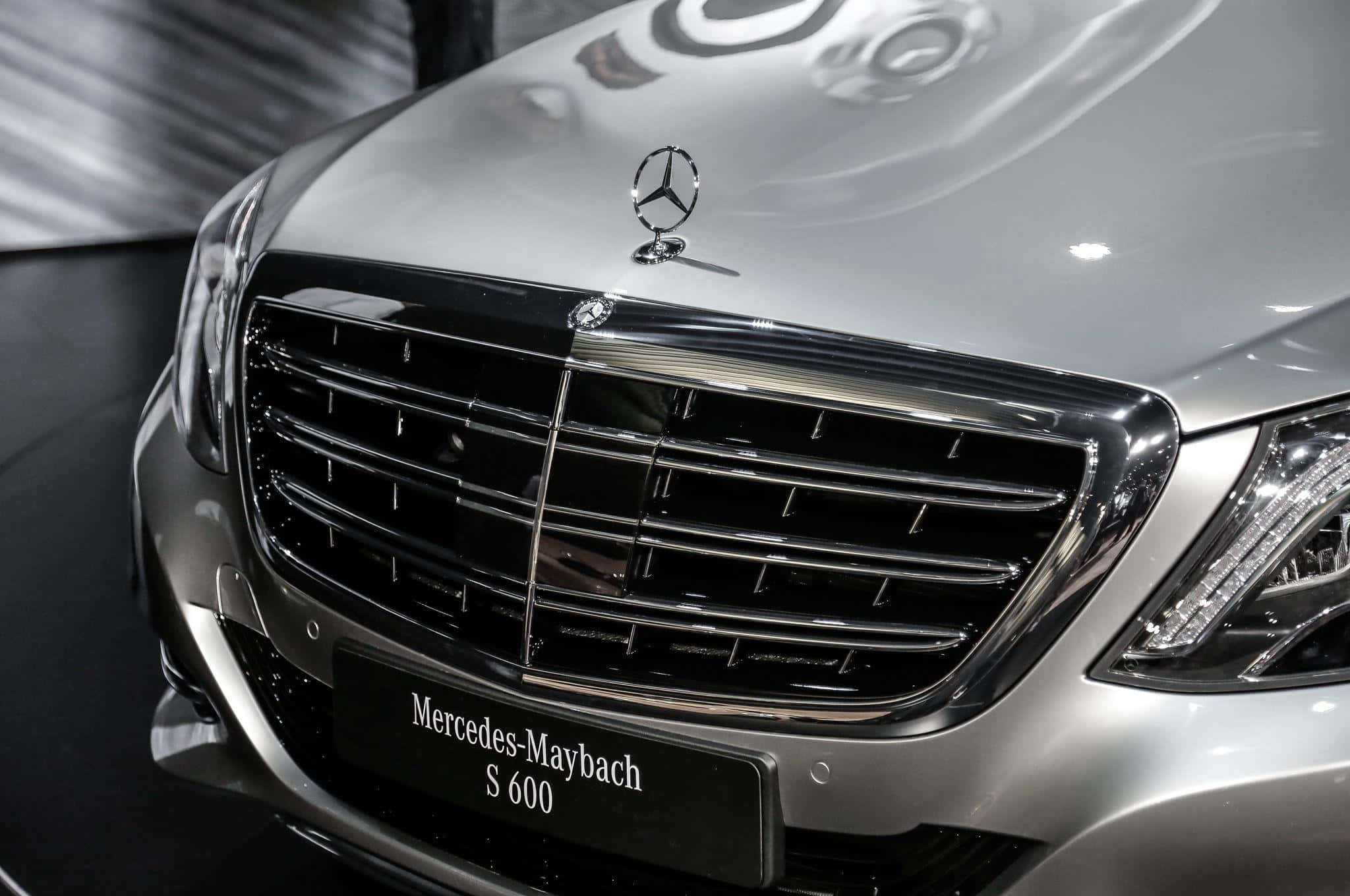 Maybach 桌布 壁紙 — 特寫一輛時尚的銀色 Mercedes-Maybach S 600，在明亮的展廳燈光下展示其鍍鉻格柵和徽章。