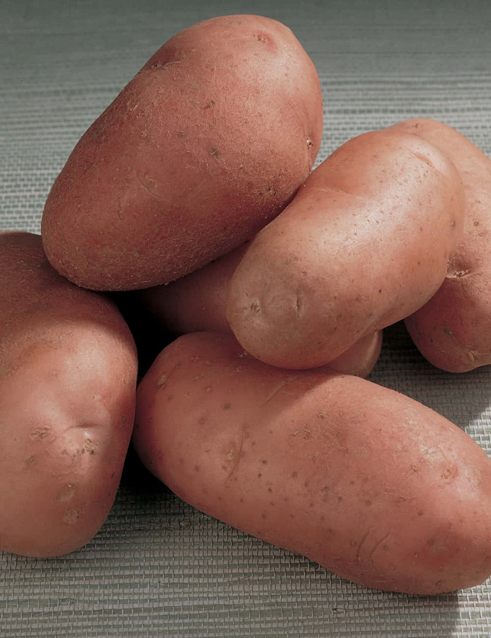 Red Potatoes 桌布 壁紙 — 特寫幾顆紅褐色馬鈴薯，置於有紋理的灰色表面上，光線柔和。
