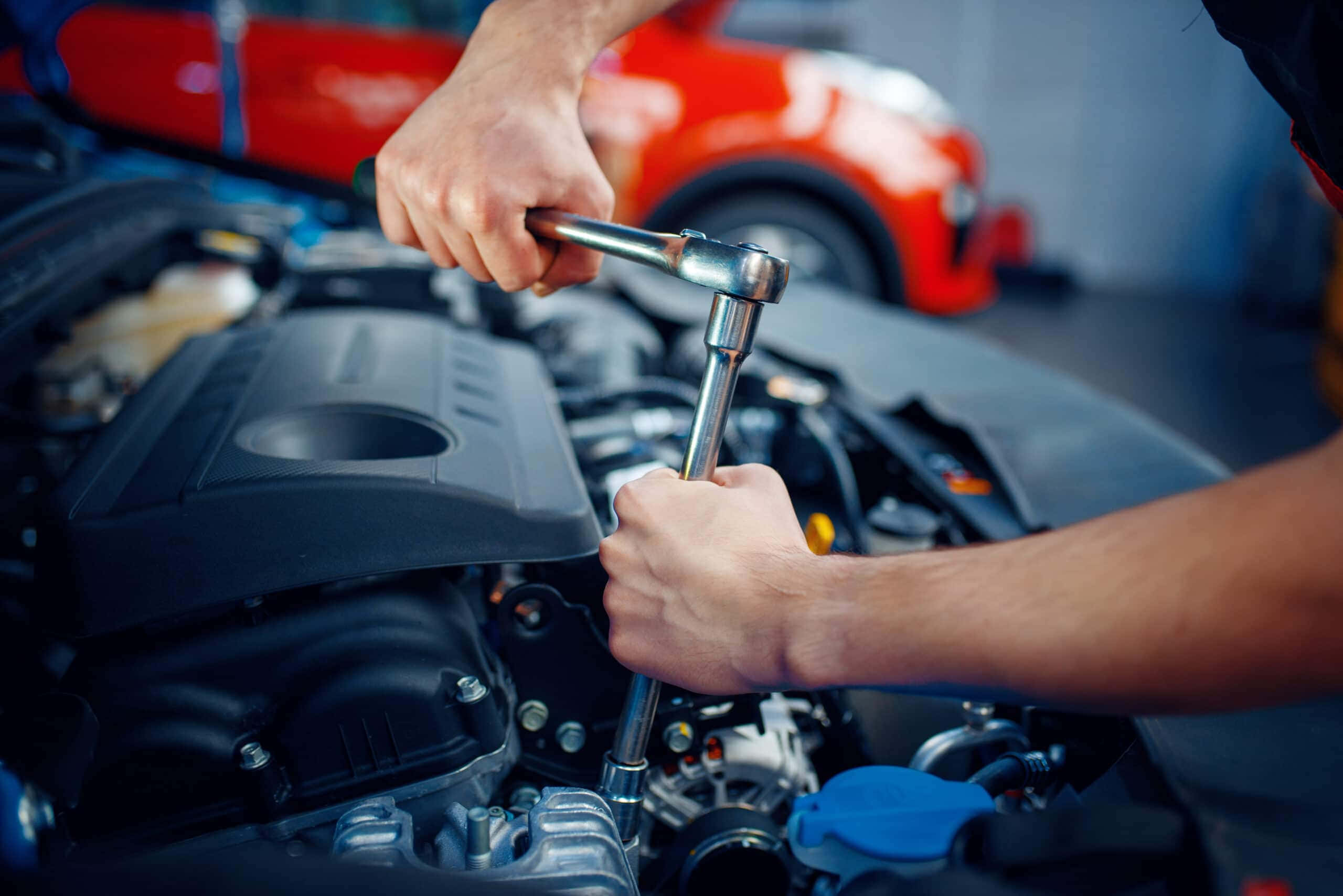 Car Repair 桌布 壁紙 — 特寫機械師的手使用棘輪扳手在汽車引擎上，背景有一輛模糊的紅色跑車。