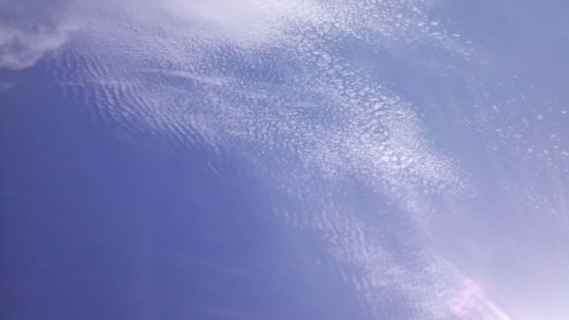 SKY-12 壁紙 — 特寫紋理藍天，帶有縷縷白雲和角落柔和嘅太陽耀斑。