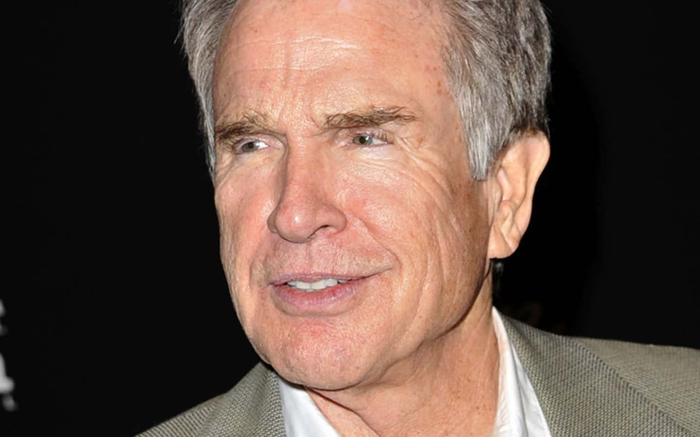 Warren Beatty 桌布 壁紙 — 特寫肖像，一位微笑的白髮老年男子穿著米色西裝，背景為黑色。