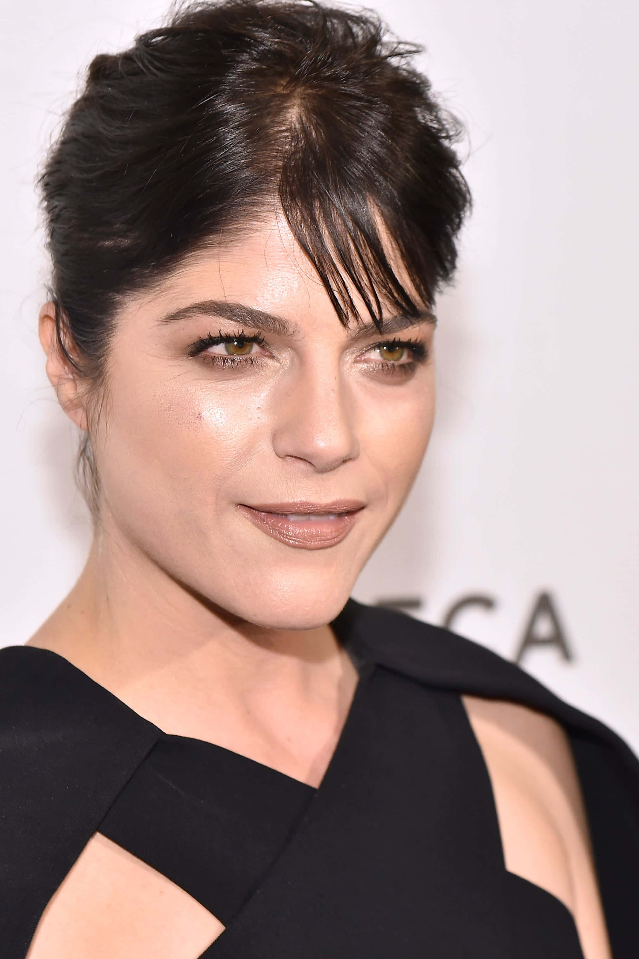 Selma Blair 桌布 壁紙 — 特寫肖像，一位深色頭髮、妝容大膽的女性，穿著黑色鏤空連衣裙，背景為白色。