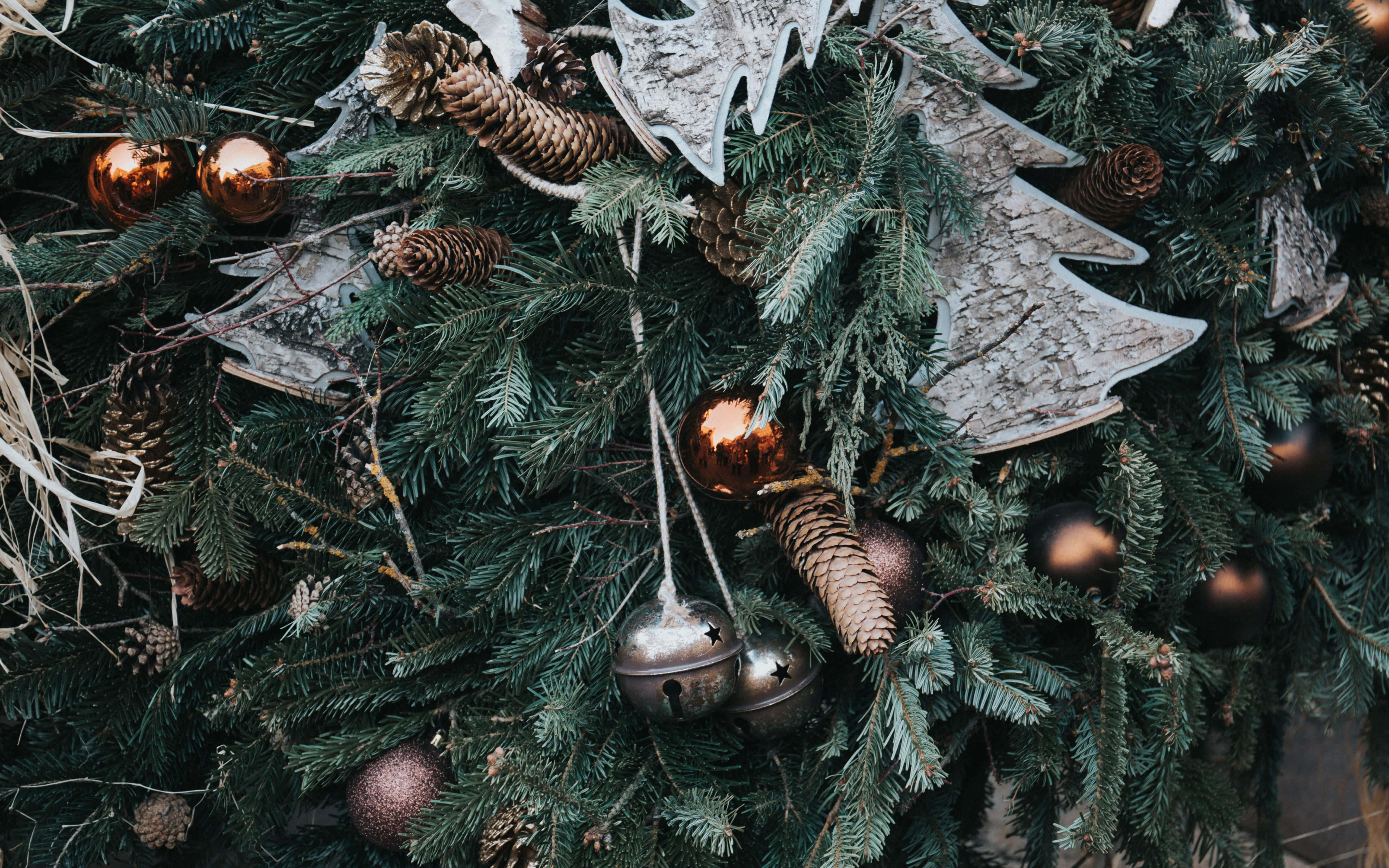 Rustic Christmas 桌布 壁紙 — 特寫鏡頭：一個茂盛的綠色聖誕花環，飾有松果、金屬鈴鐺和質樸的木製樹形剪影。