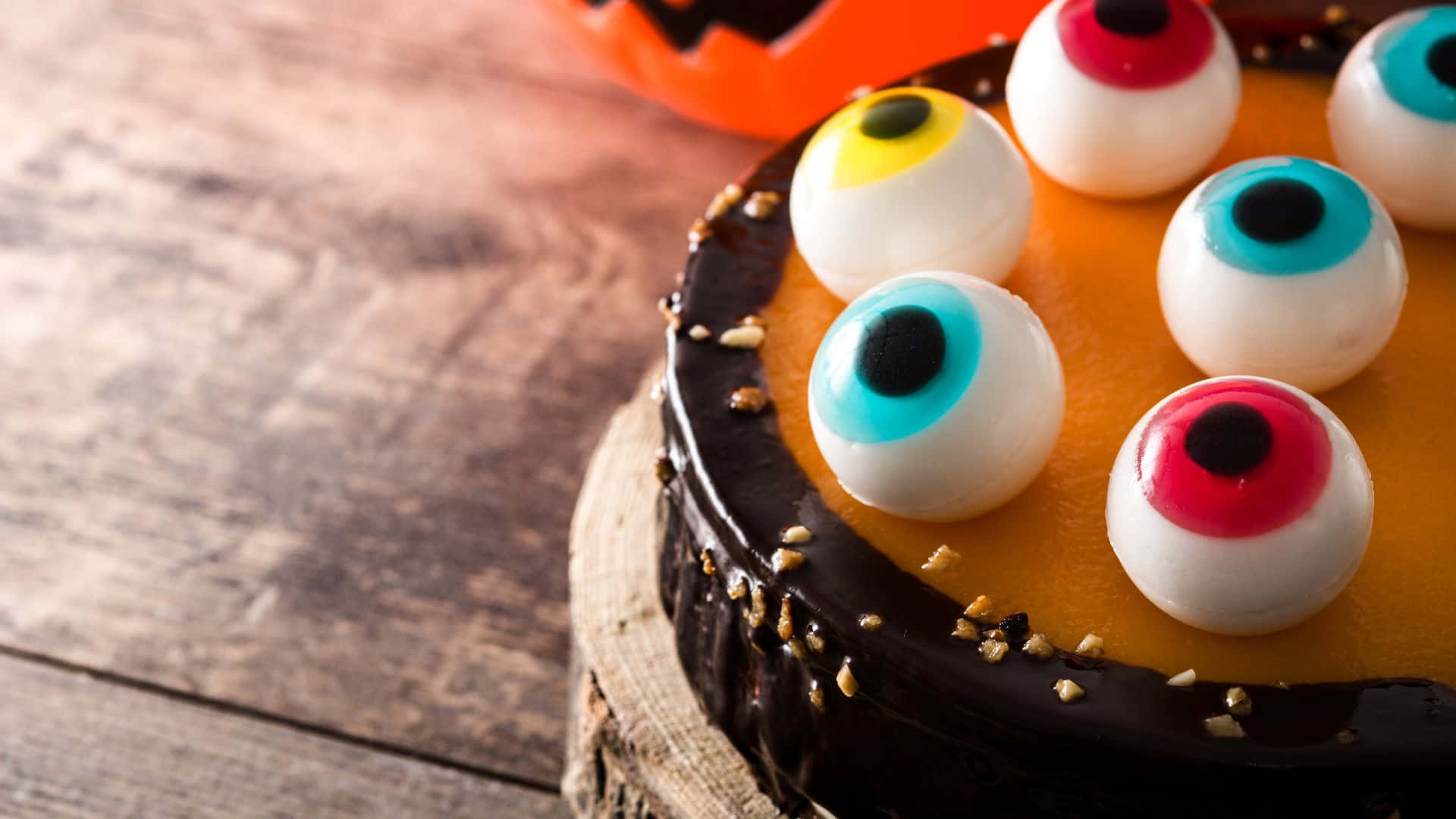 Halloween Cake 桌布 壁紙 — 特寫鏡頭：一個萬聖節蛋糕，上面鋪滿色彩繽紛的糖果眼睛和朱古力甘納許，放在質樸的木板上。