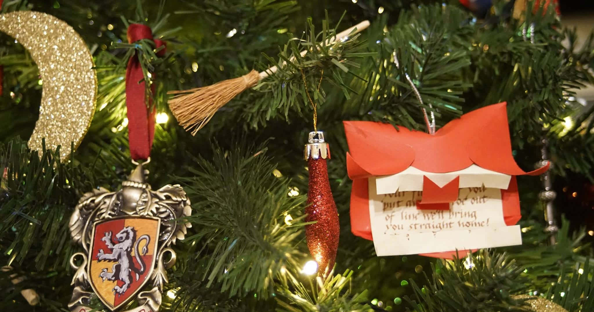 Harry Potter Christmas 桌布 壁紙 — 特寫鏡頭：一棵聖誕樹，裝飾著哈利波特主題的飾品，包括掃帚徽章和紅色蝴蝶結便條。