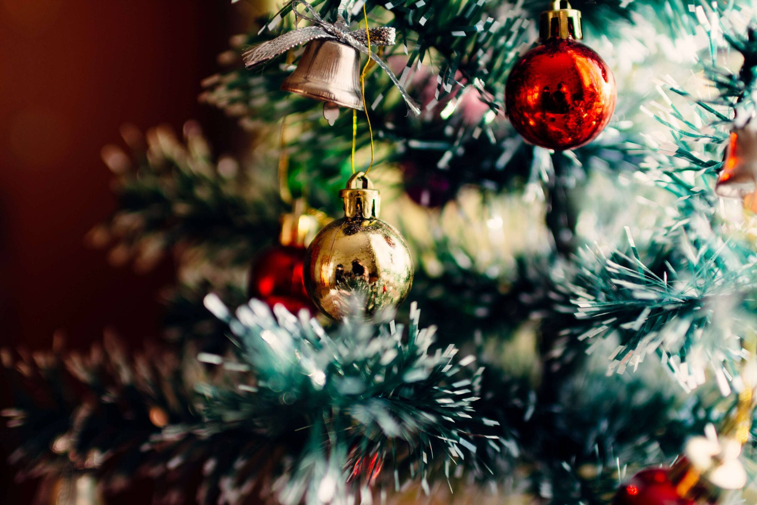 Christmas Balls 桌布 壁紙 — 特寫鏡頭：一棵裝飾著紅色和金色飾品以及一個銀色鈴鐺懸掛在綠色樹枝間的聖誕樹。