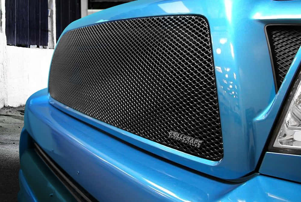 Car Grill 桌布 壁紙 — 特寫鏡頭：一輛鮮藍色卡車的前格柵，帶有黑色網格和「GILLCRAFT」品牌標誌，在明亮的日光下。