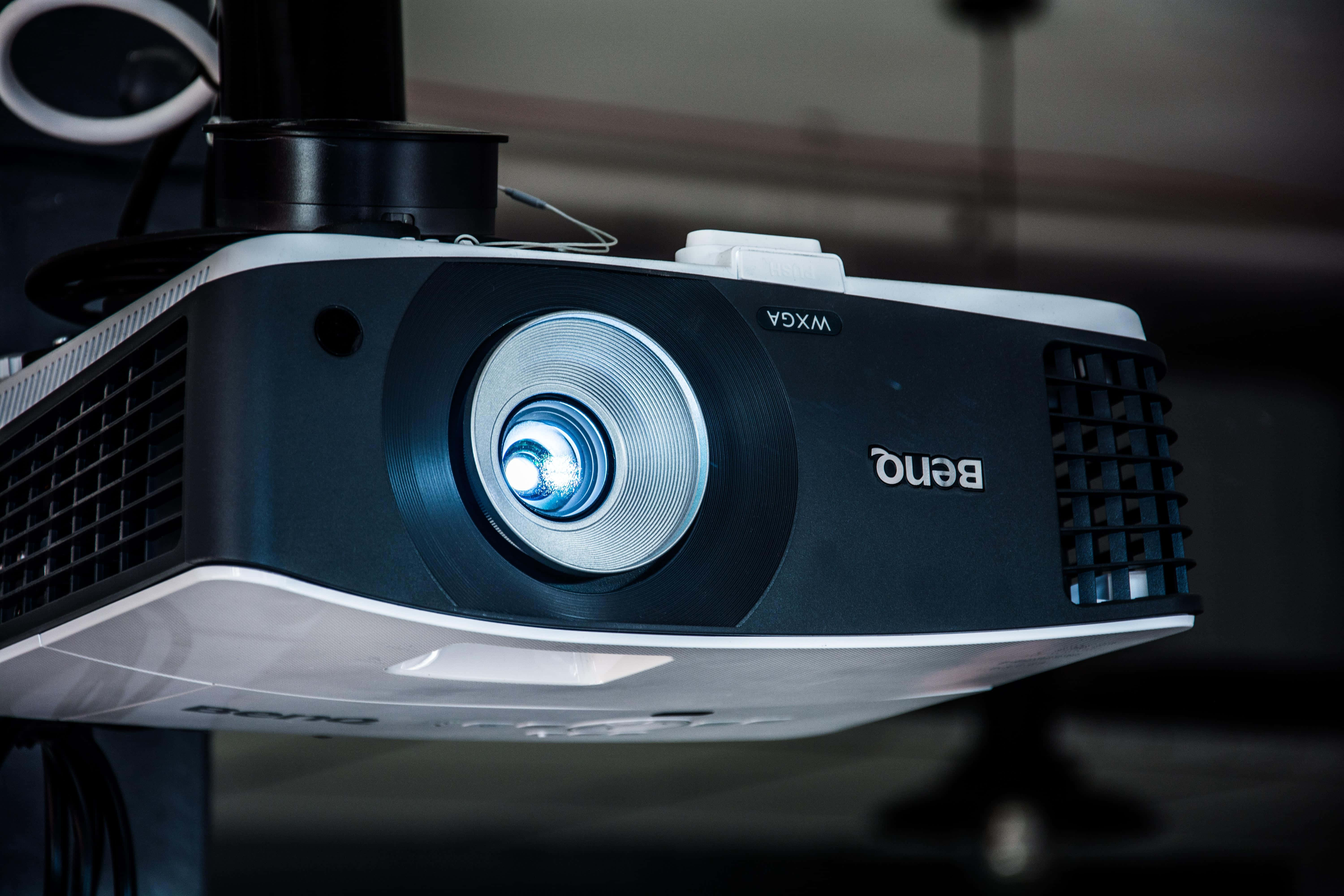 4K Projector 桌布 壁紙 — 特寫鏡頭：一部BenQ投影機，裝有發出藍光的鏡頭，安裝在昏暗房間的支架上。
