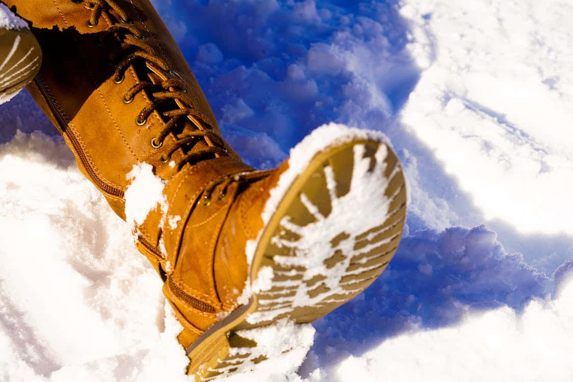 Snowshoes 桌布 壁紙 — 特寫鏡頭：啡色冬季靴子踏進新鮮積雪，背景是明亮的藍天。