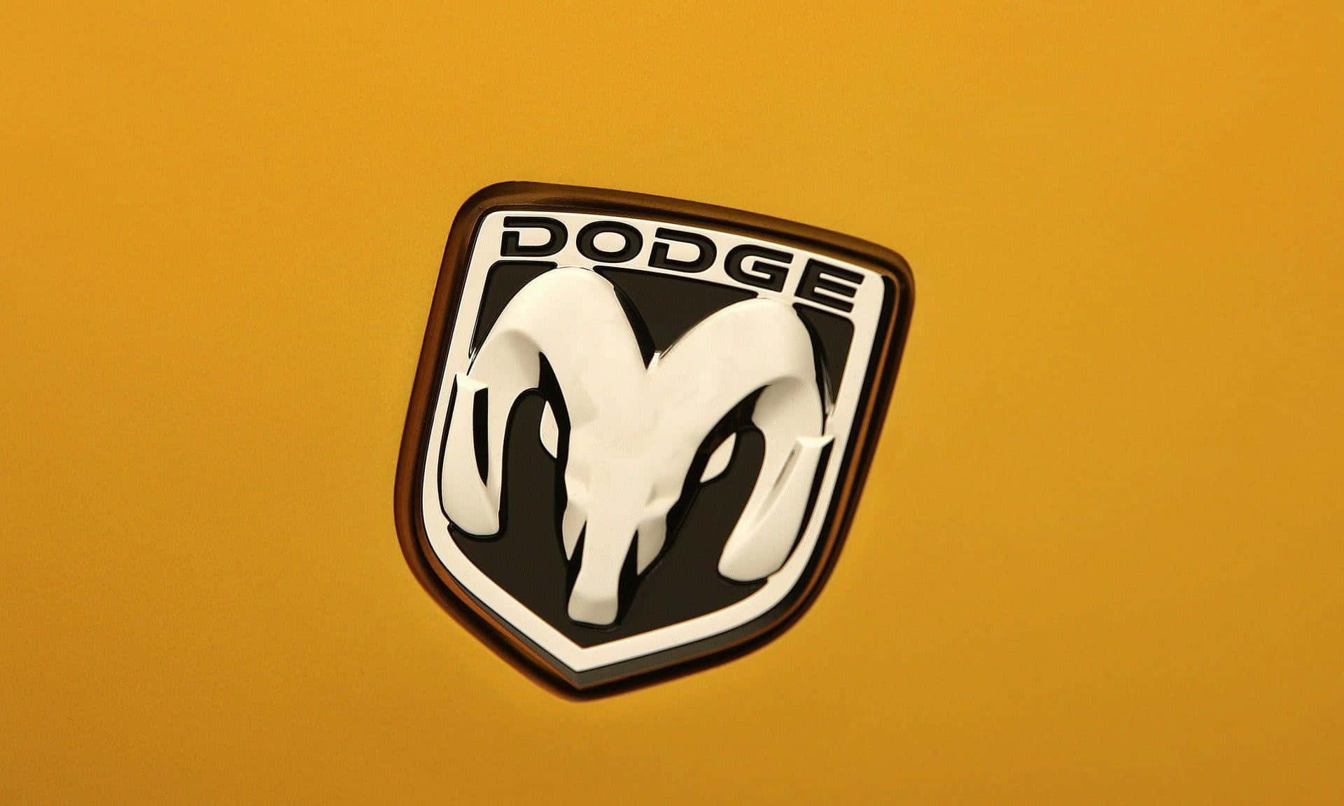Car Logo 桌布 壁紙 — 特寫鏡頭：在明亮日光下，鮮黃色車頭蓋上閃亮的 Dodge ram 標誌。