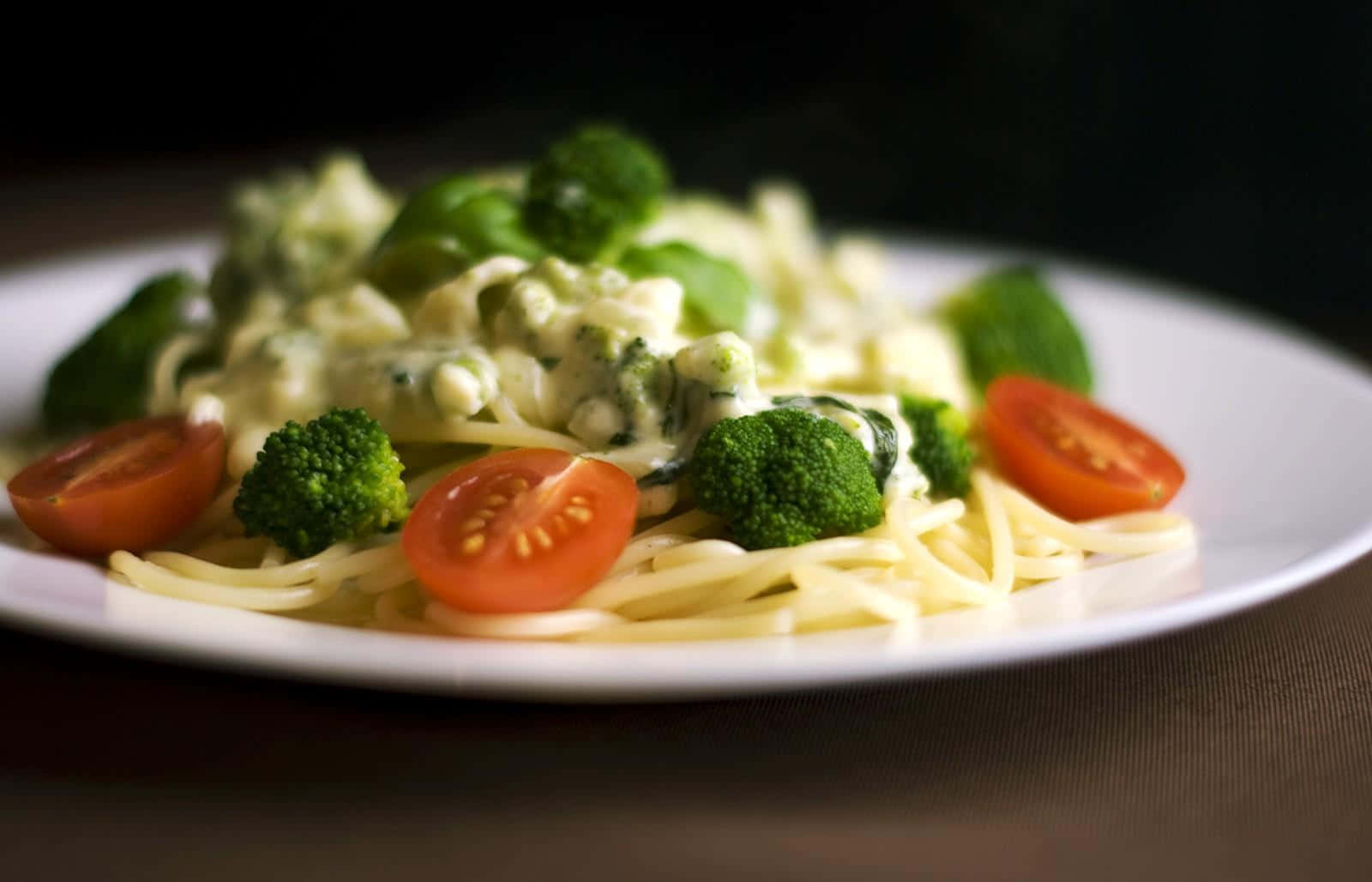 Pasta 桌布 壁紙 — 特寫鏡頭：奶油意粉配西蘭花及車厘茄，置於白色碟上，背景深色。