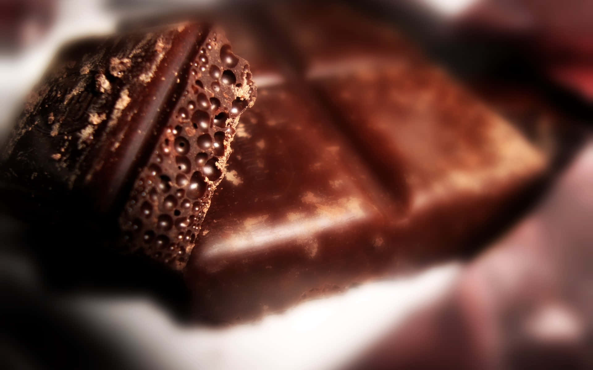 Dark Chocolate 桌布 壁紙 — 特寫鏡頭，展示一塊濃郁的黑巧克力棒，表面紋理豐富、帶有氣泡，並有光澤感。