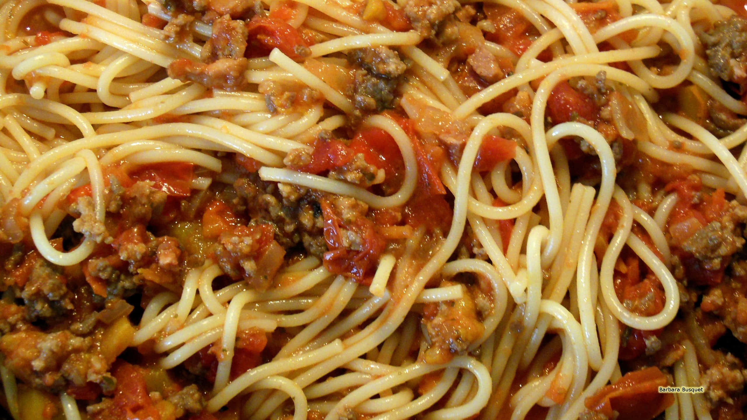Pasta 桌布 壁紙 — 特寫鏡頭：意大利麵配上濃郁番茄醬和肉碎，在溫暖燈光下閃閃發光。