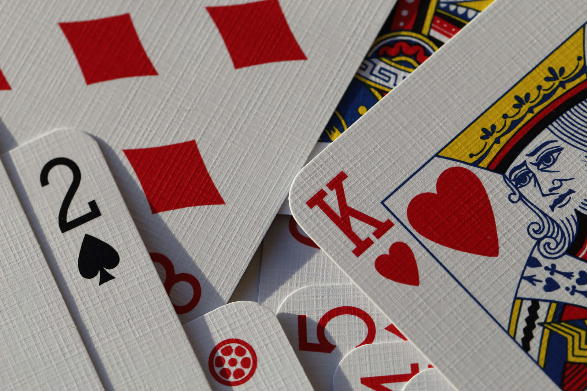 Playing Cards 桌布 壁紙 — 特寫鏡頭，散落的撲克牌，包括紅心K和黑桃2，在明亮的陽光下。