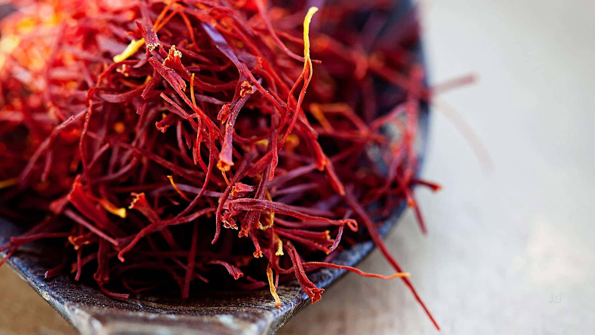 Saffron 桌布 壁紙 — 特寫鏡頭：深色陶瓷碗中溢出鮮豔的紅色番紅花絲，背景為柔和的白色。