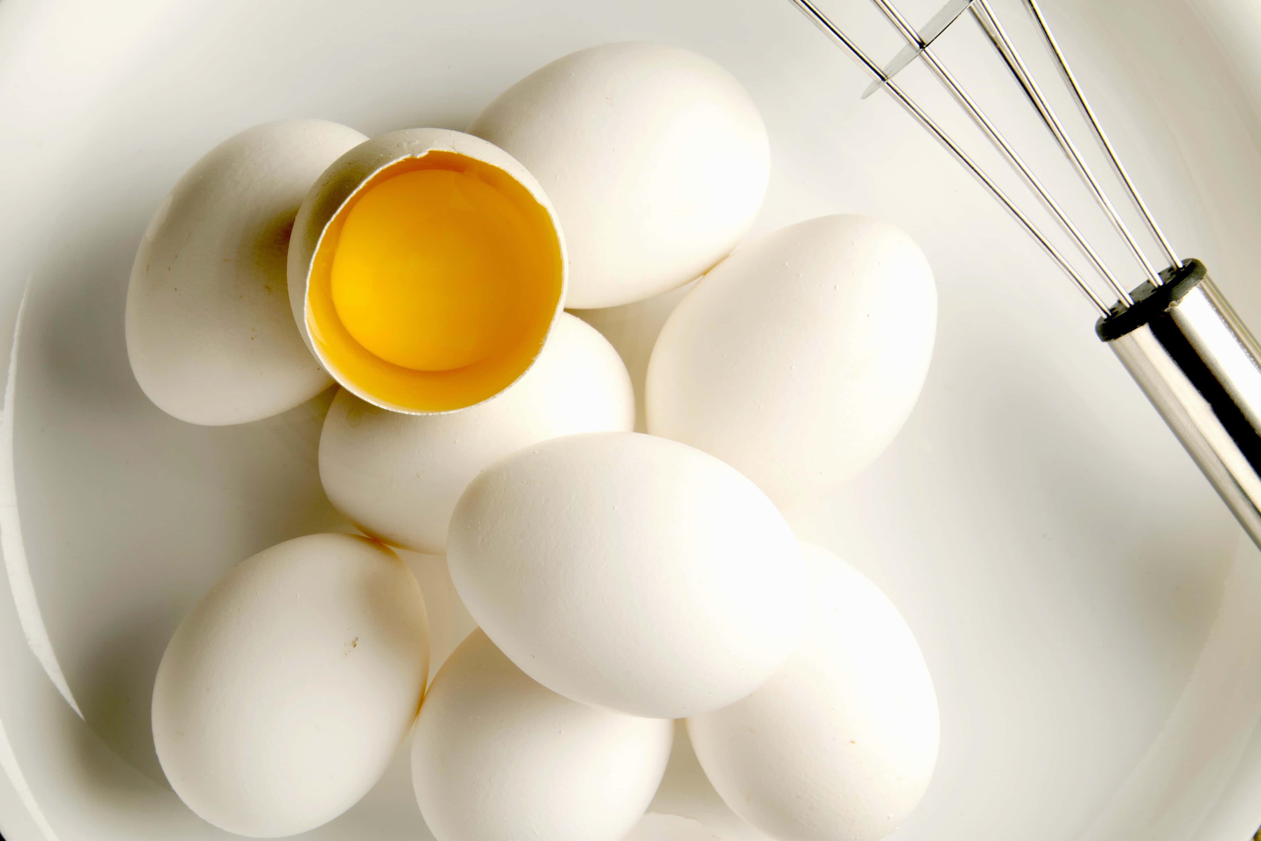 Egg White 桌布 壁紙 — 特寫鏡頭：碗中的白色雞蛋，其中一個裂開露出亮黃色的蛋黃，旁邊有一個金屬打蛋器。