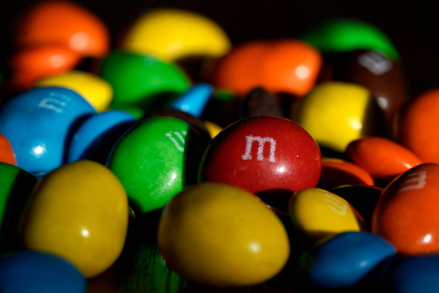 Chocolate 桌布 壁紙 — 特寫鏡頭：色彩繽紛的M&M's糖果，帶有光澤外殼和白色「m」標誌，背景為深色。