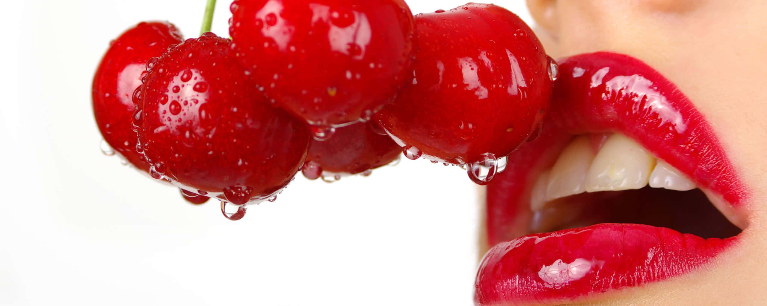 Cherry 桌布 壁紙 — 特寫鏡頭：閃亮紅櫻桃帶有水珠，被塗有相配紅色唇膏的女性嘴唇咬住。