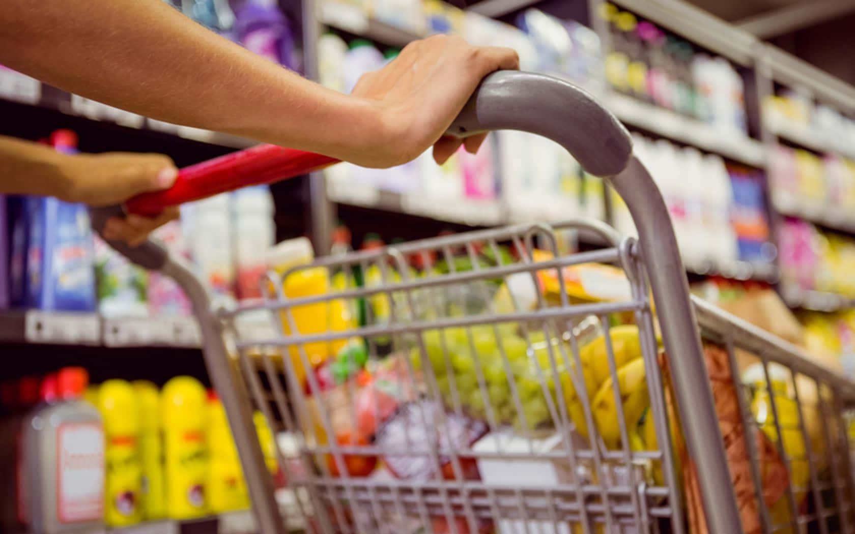 Grocery Store 桌布 壁紙 — 特寫鏡頭：雙手推著裝滿雜貨的購物車，穿過燈光明亮的超市通道。