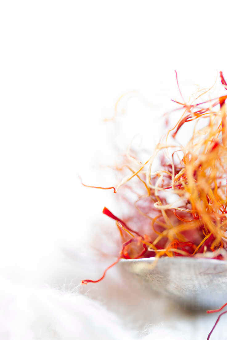 Saffron 桌布 壁紙 — 特寫鏡頭，鮮豔的橙色番紅花絲線放在白色表面上，背景柔和散景。