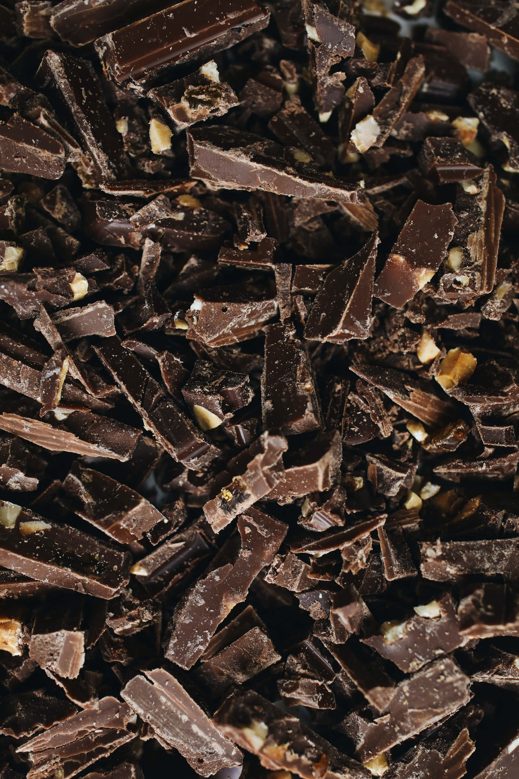 Dark Chocolate 桌布 壁紙 — 特寫鏡頭展示濃郁黑朱古力塊，上面鑲嵌著可見的堅果碎，營造出奢華的紋理表面。