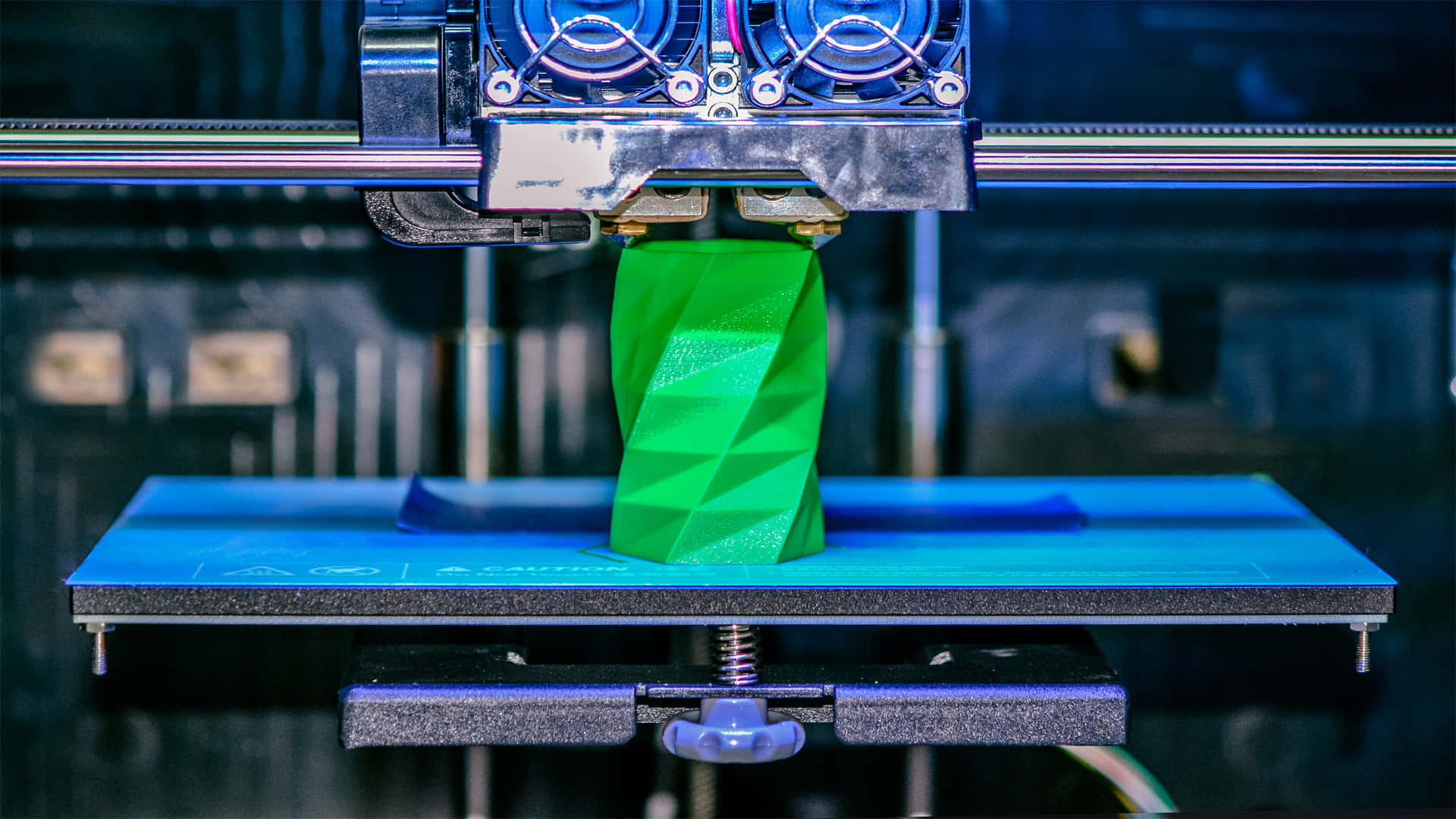 3d Printer 桌布 壁紙 — 特寫鏡頭顯示3D打印機在藍色打印平台上擠出鮮綠色線材，構建幾何螺旋物體。