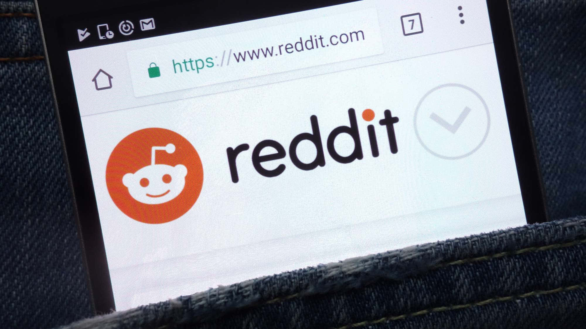reddit 桌布 壁紙 — 特寫鏡頭顯示一部智能手機，屏幕上展示Reddit首頁，標誌和網址清晰可見，手機放在牛仔褲口袋中。