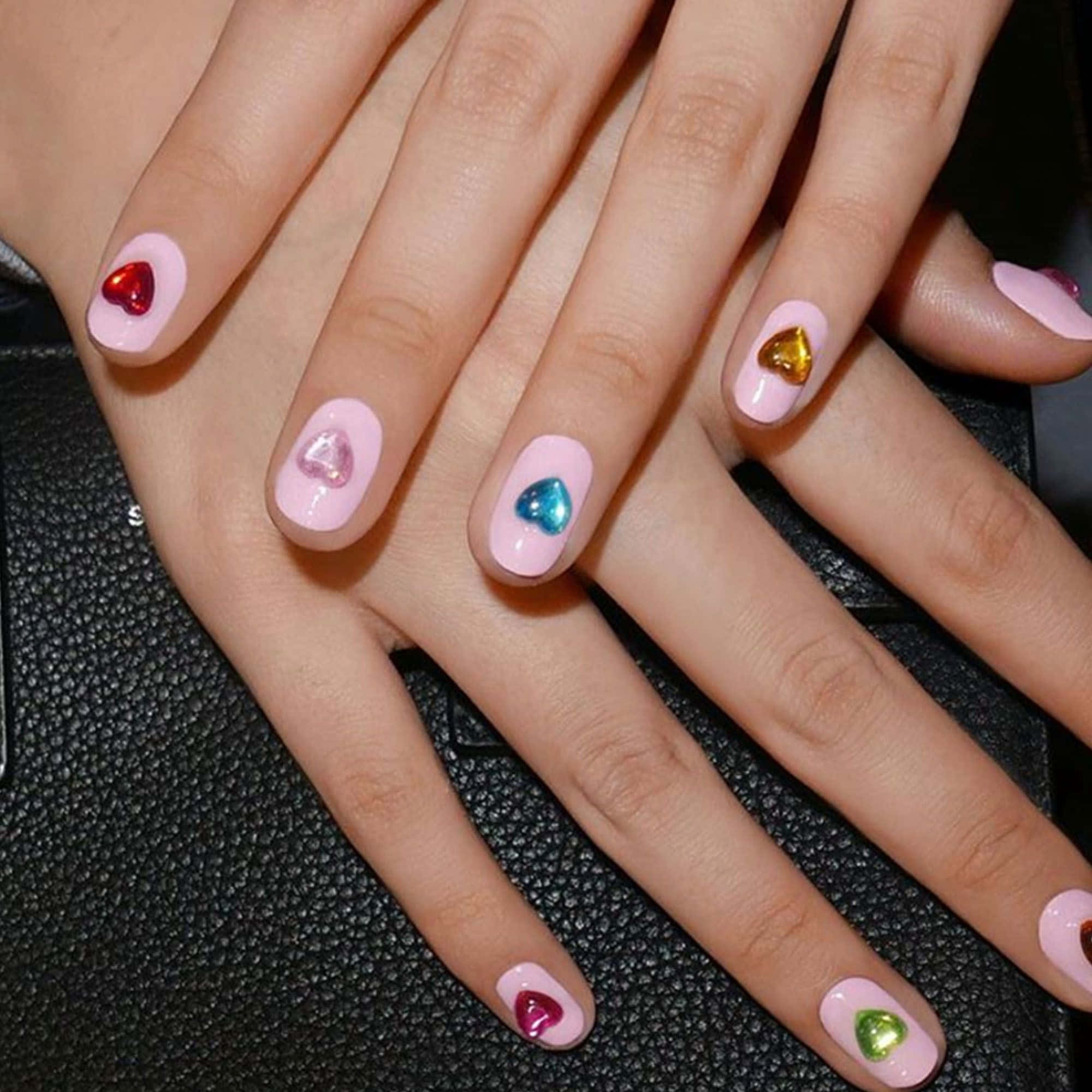 Spring Nails 桌布 壁紙 — 特寫雙手，帶有粉彩粉紅色指甲，飾以彩色心形寶石，背景為黑色紋理。